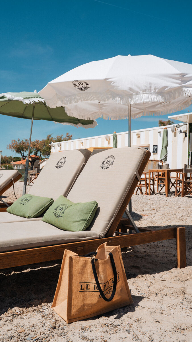 Transats en teck et parasol blanc à franges sur le sable des Lecques